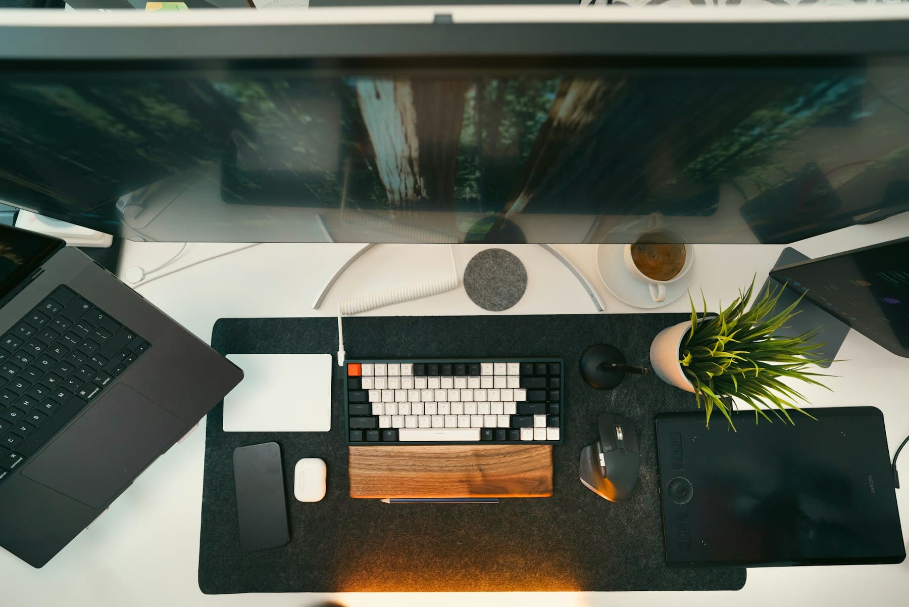Overhead view of a tidy desk with a mechanical keyboard, wooden wrist rest, plant, coffee and laptop