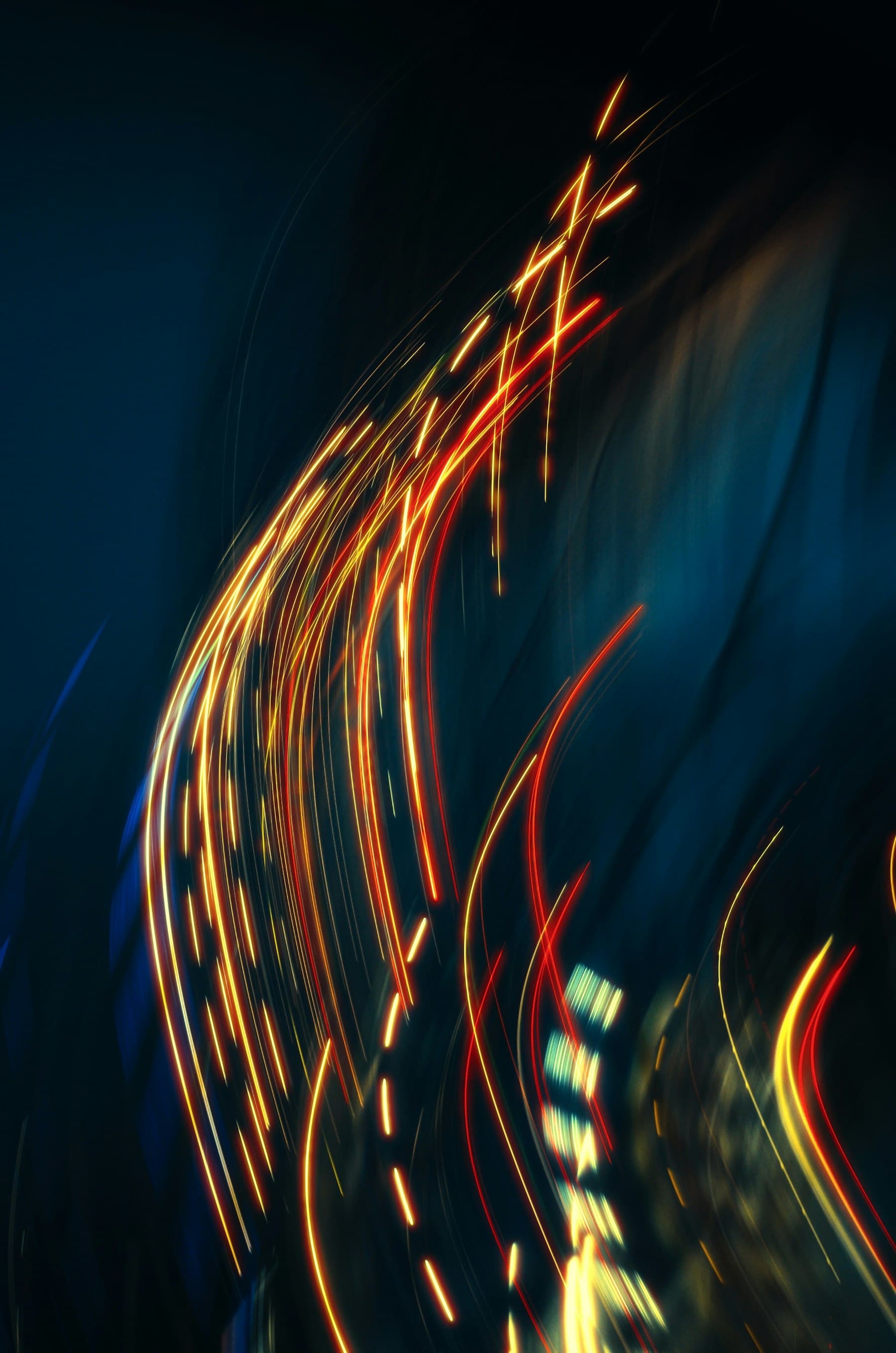 Abstract long-exposure photograph of sweeping gold and red light trails against a dark blue-toned background, symbolizing continuous operation over time